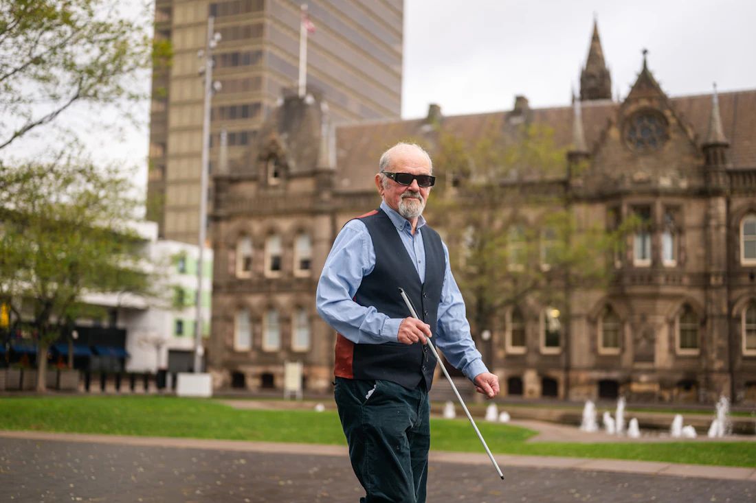 An older person walks confidently using a white cane, an example of an assistive device that supports safe mobility