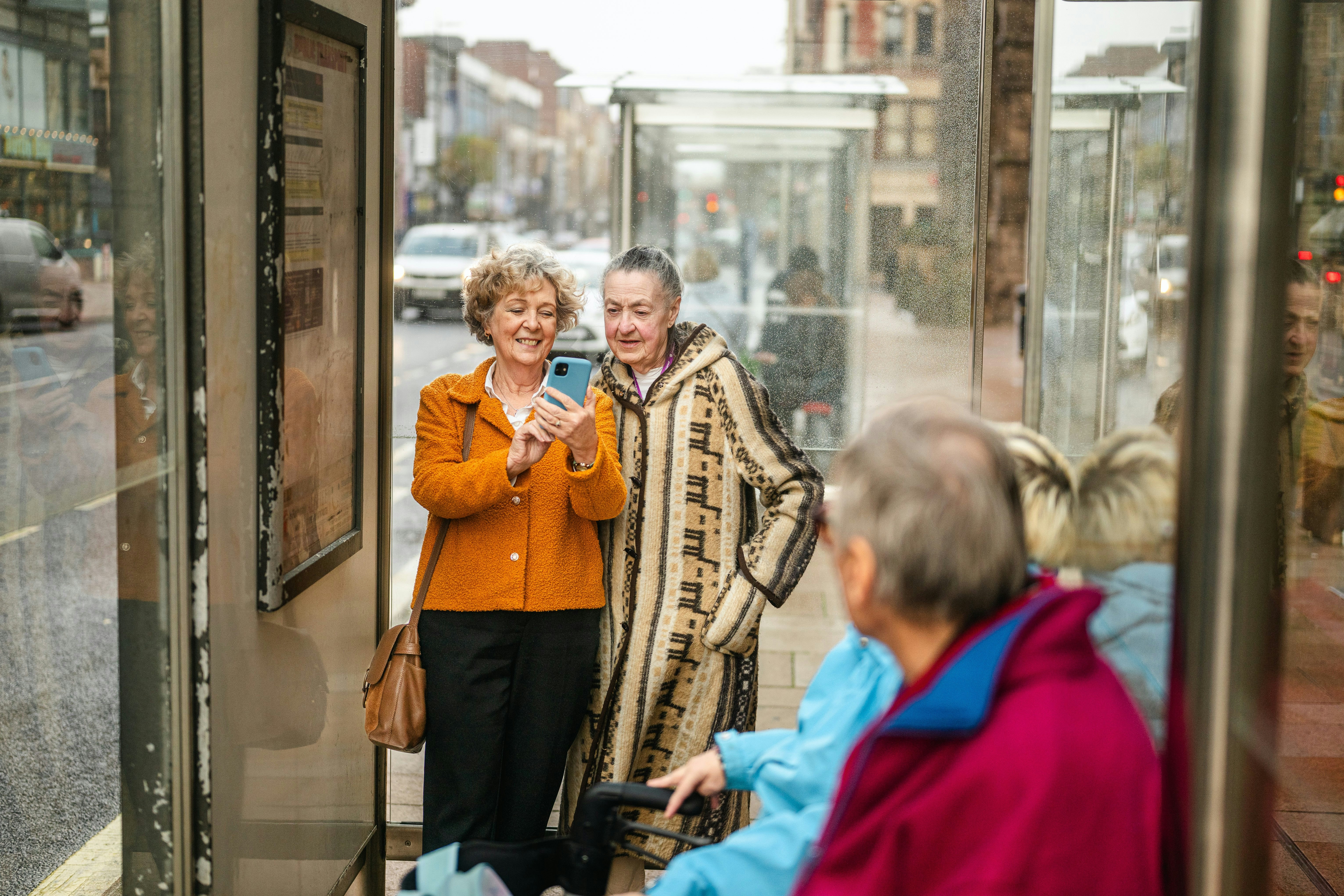 Two women looking at a smartphone at a bus stop.