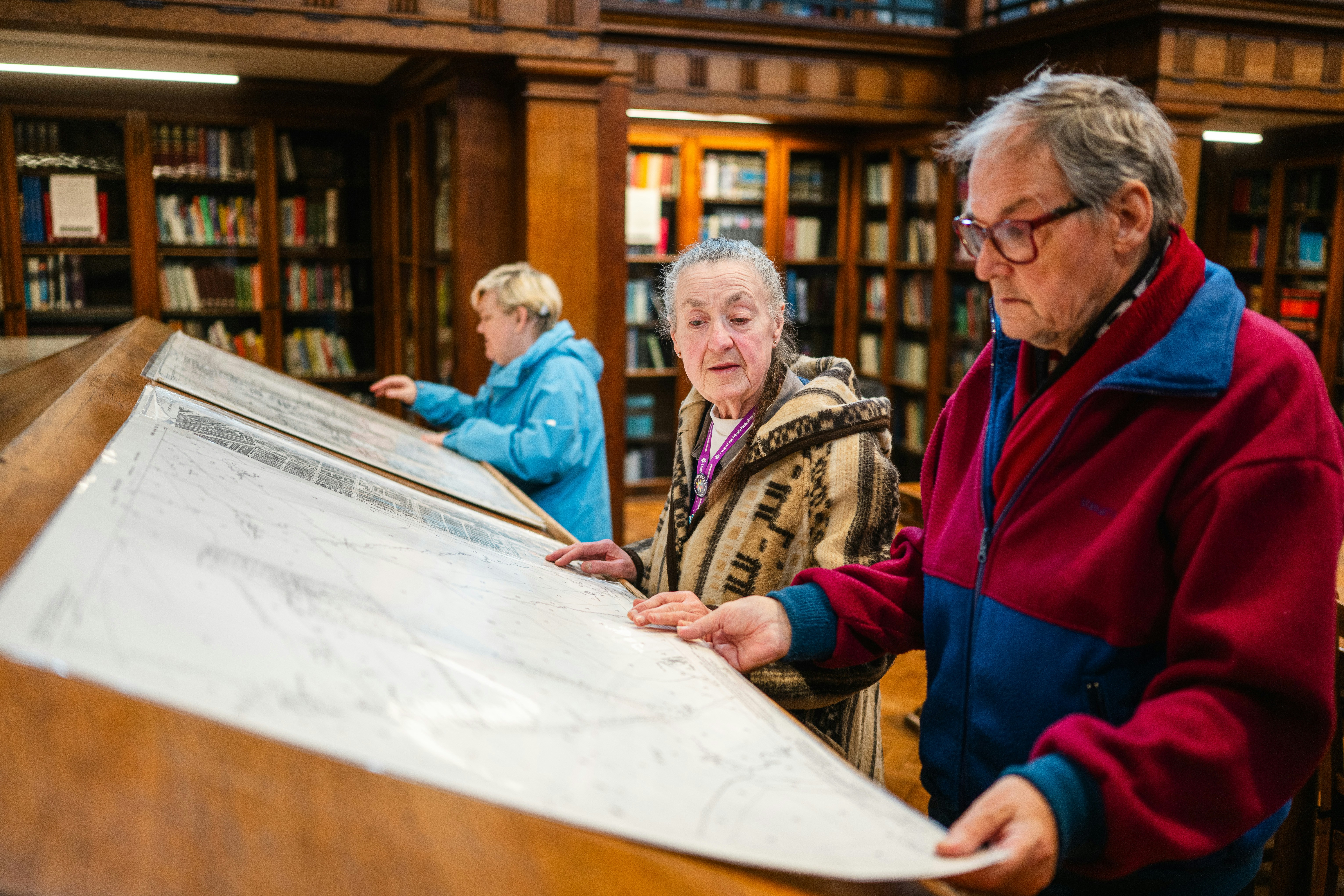 Elderly people examining large documents in library