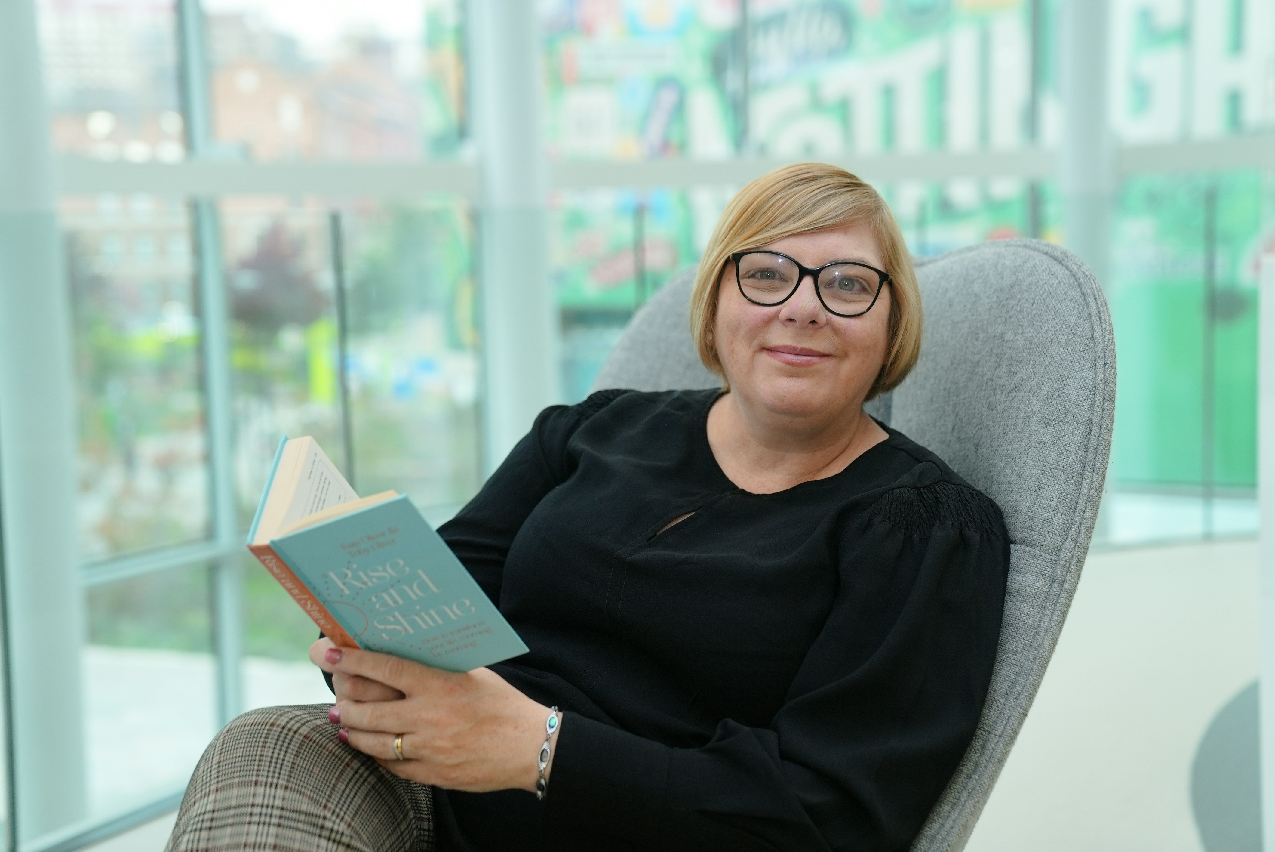 A woman sits in a chair reading a book.