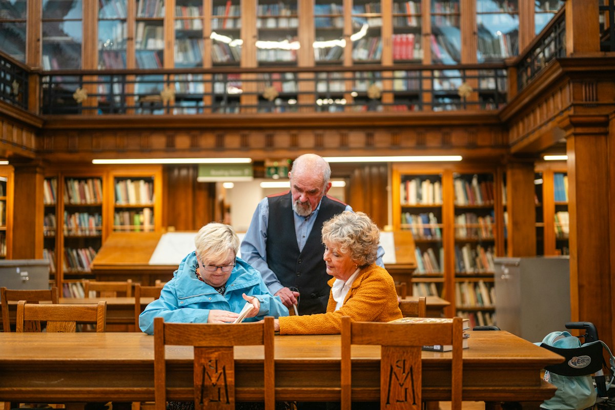 Three parents discussing a volunteer program at a wooden table in a school library.