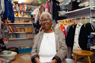 Elderly woman smiling in a room filled with clothes.