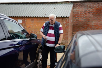 An older man stands between two cars