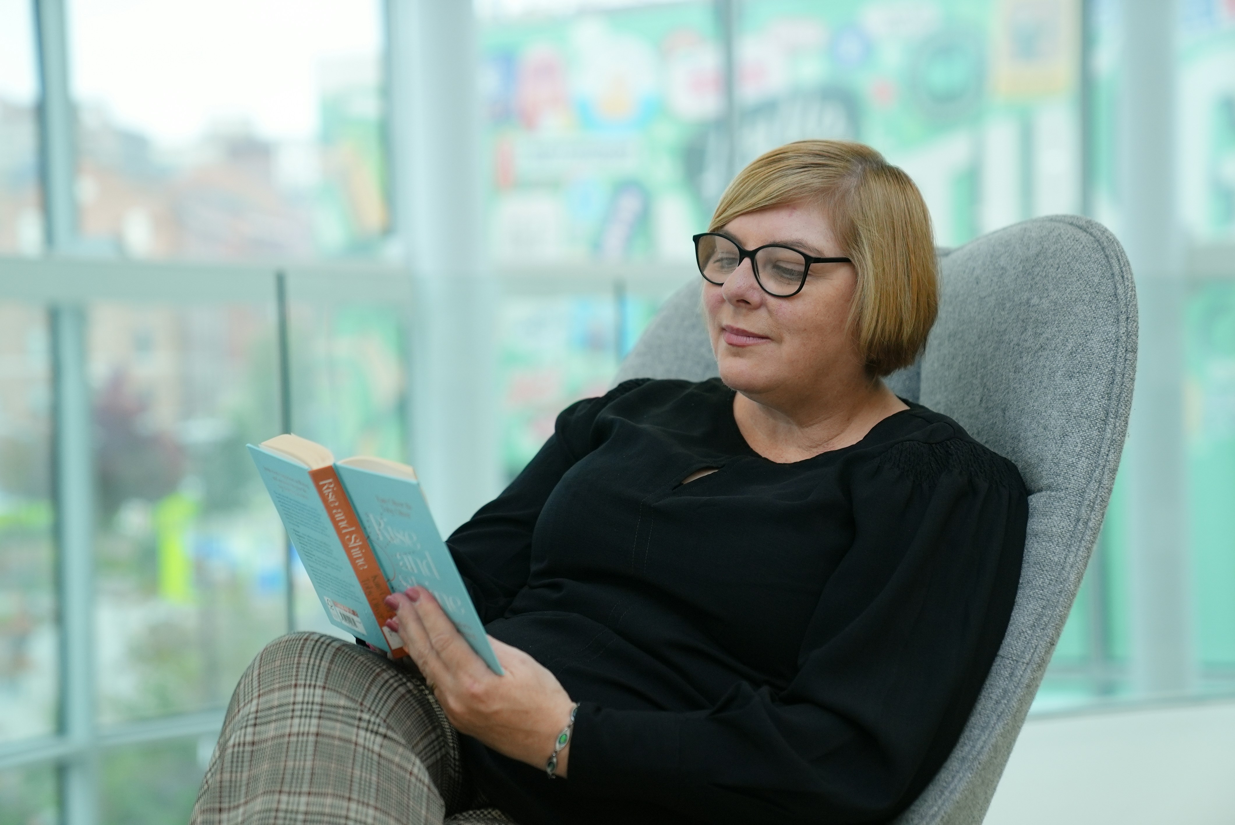 Woman wearing glasses reading a book in a chair