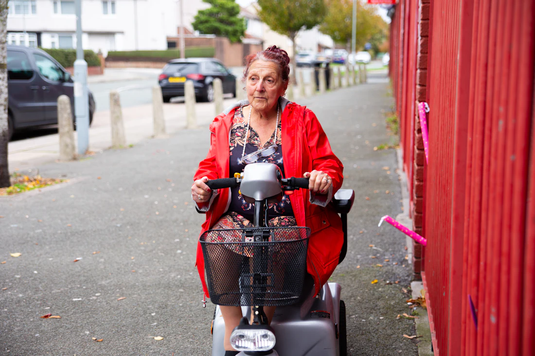 An older woman using a mobility scooter outdoors, representing a resident whose daily needs depend on consistent staff support