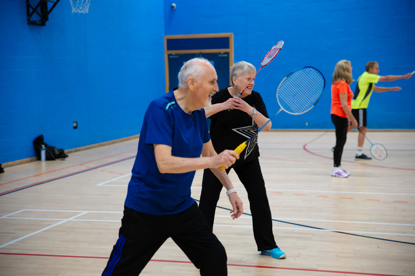 Seniors mid-rally on a badminton court