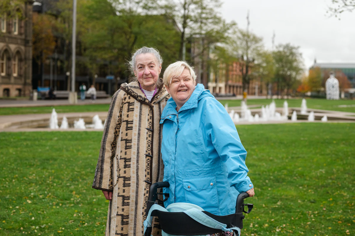 Two smiling older women standing together in a sunlit park