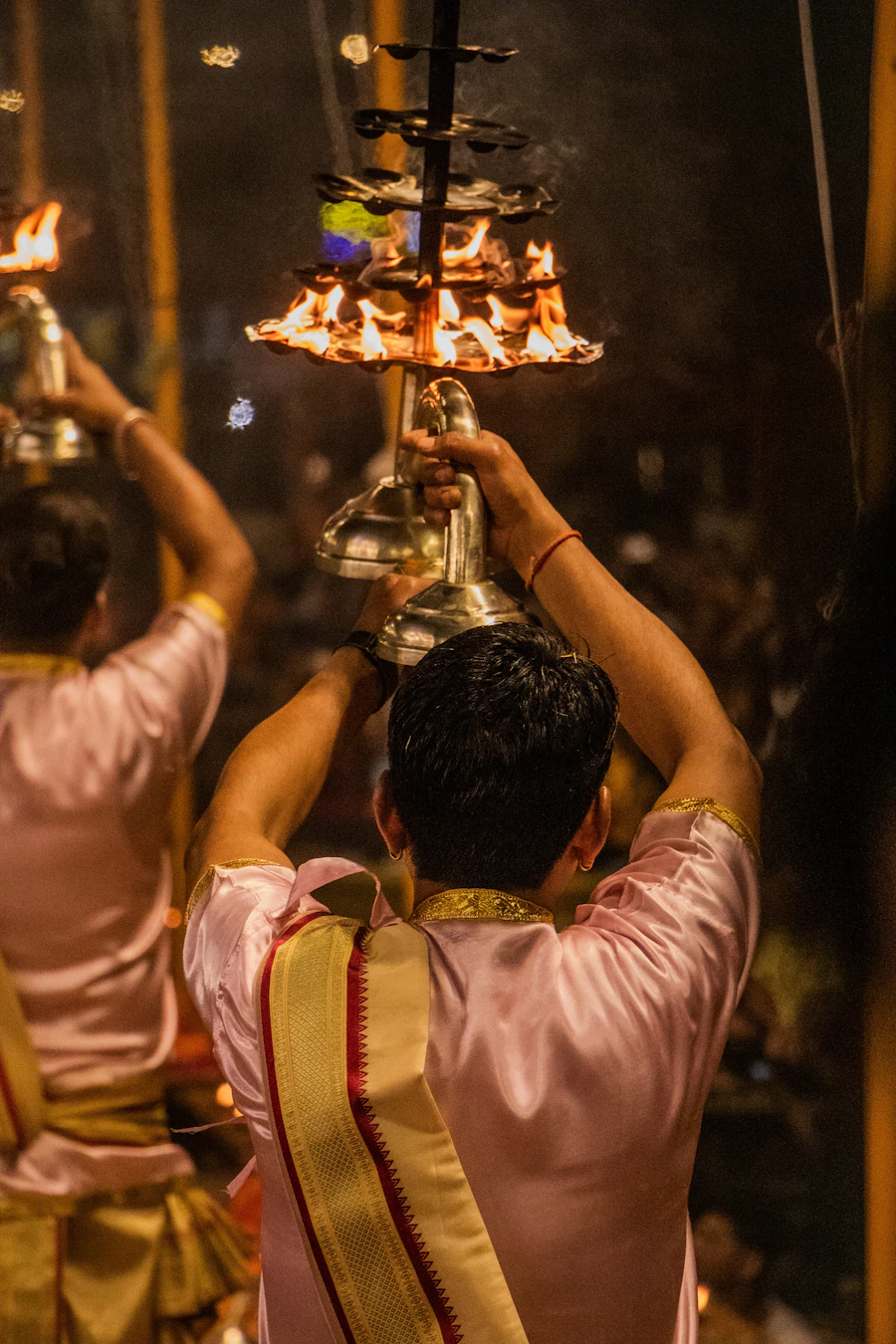 Priests performing evening aarti with a multi-tiered brass lamp