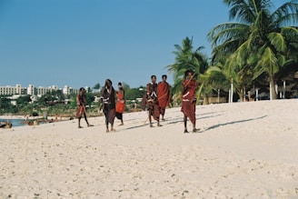 People in traditional clothing walking on a sandy beach.