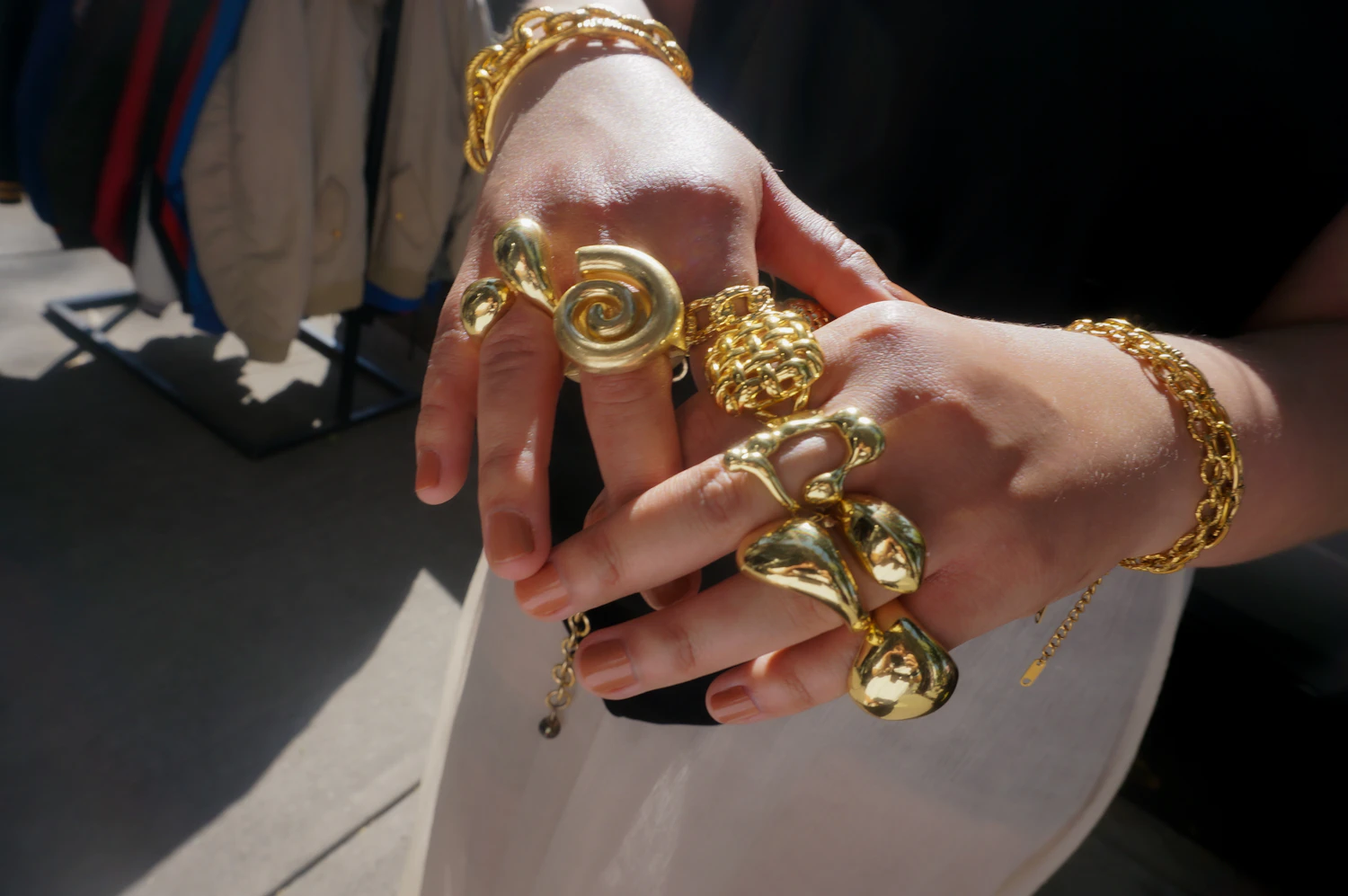 One hand wearing six heavy gold rings of different widths across four fingers, in bright daylight