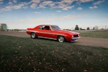 A red vintage chevrolet camaro drives on a road.