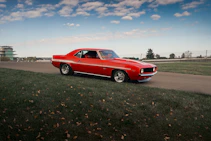 A red vintage chevrolet camaro drives on a road.
