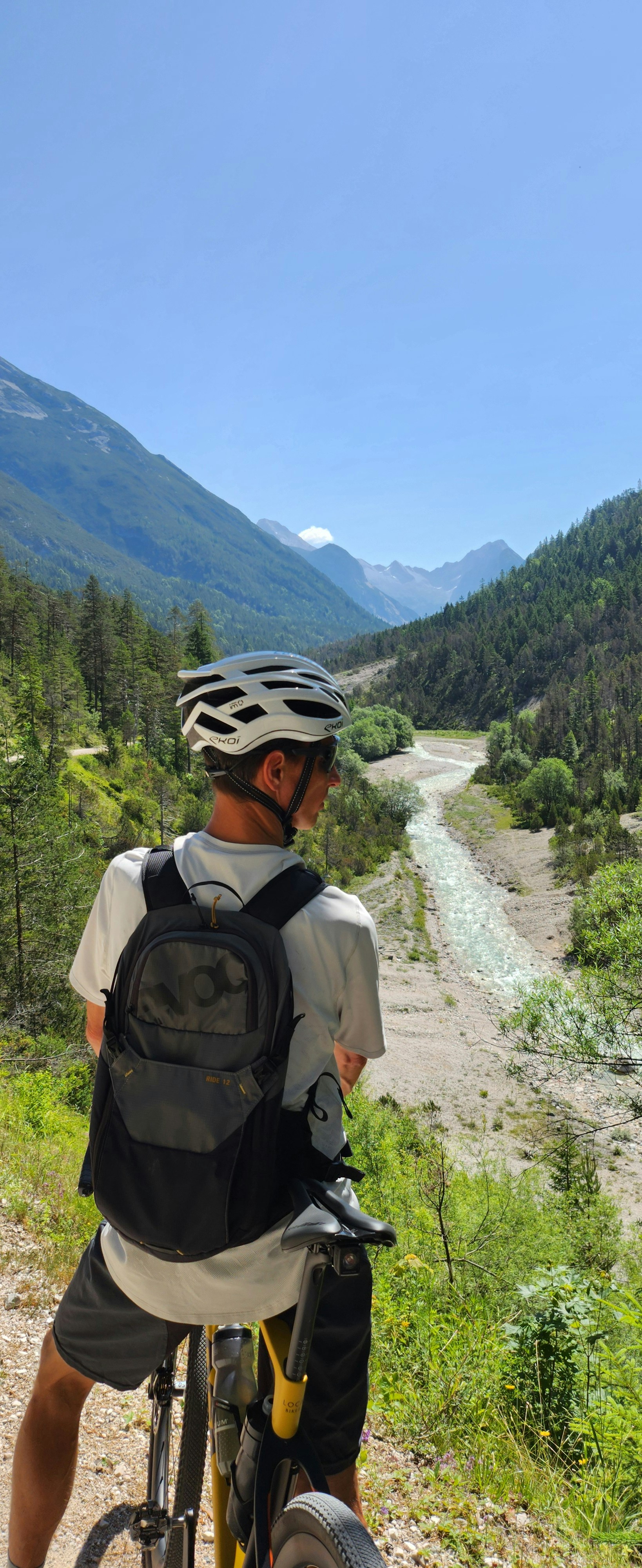 A cyclist in a white helmet and backpack overlooking a river valley