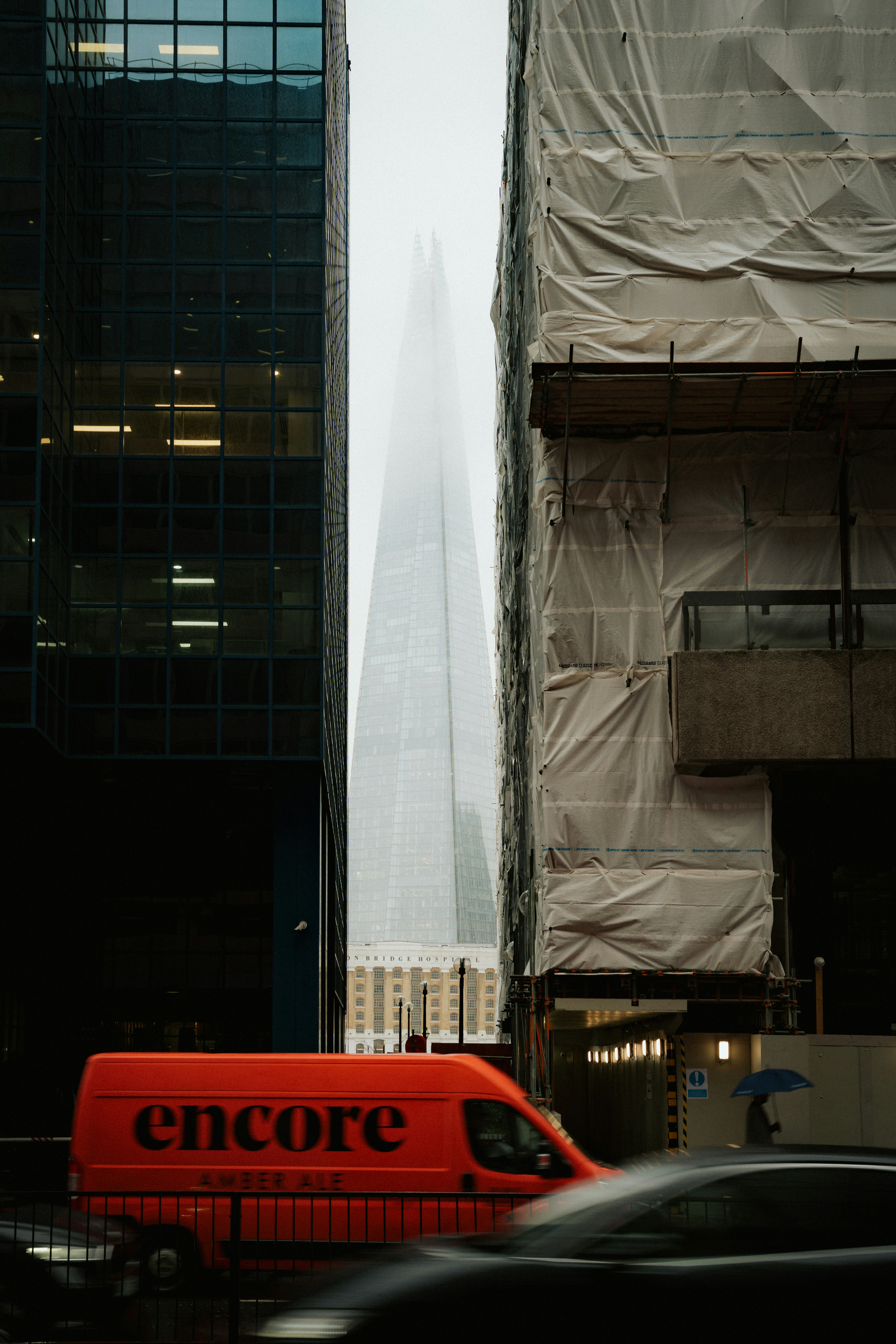 Orange van passes between modern buildings with skyscraper.
