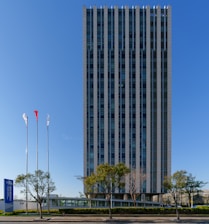 Modern skyscraper with flags under a clear blue sky.