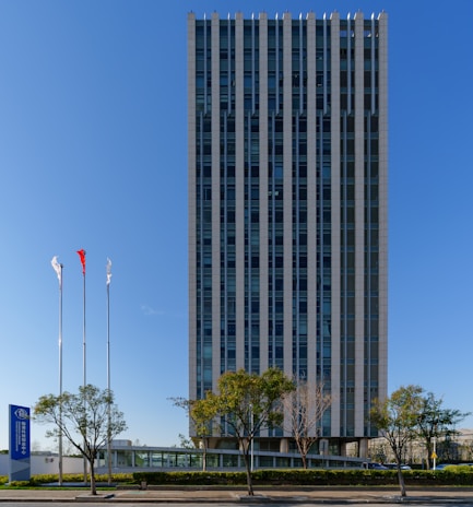 Modern skyscraper with flags under a clear blue sky.
