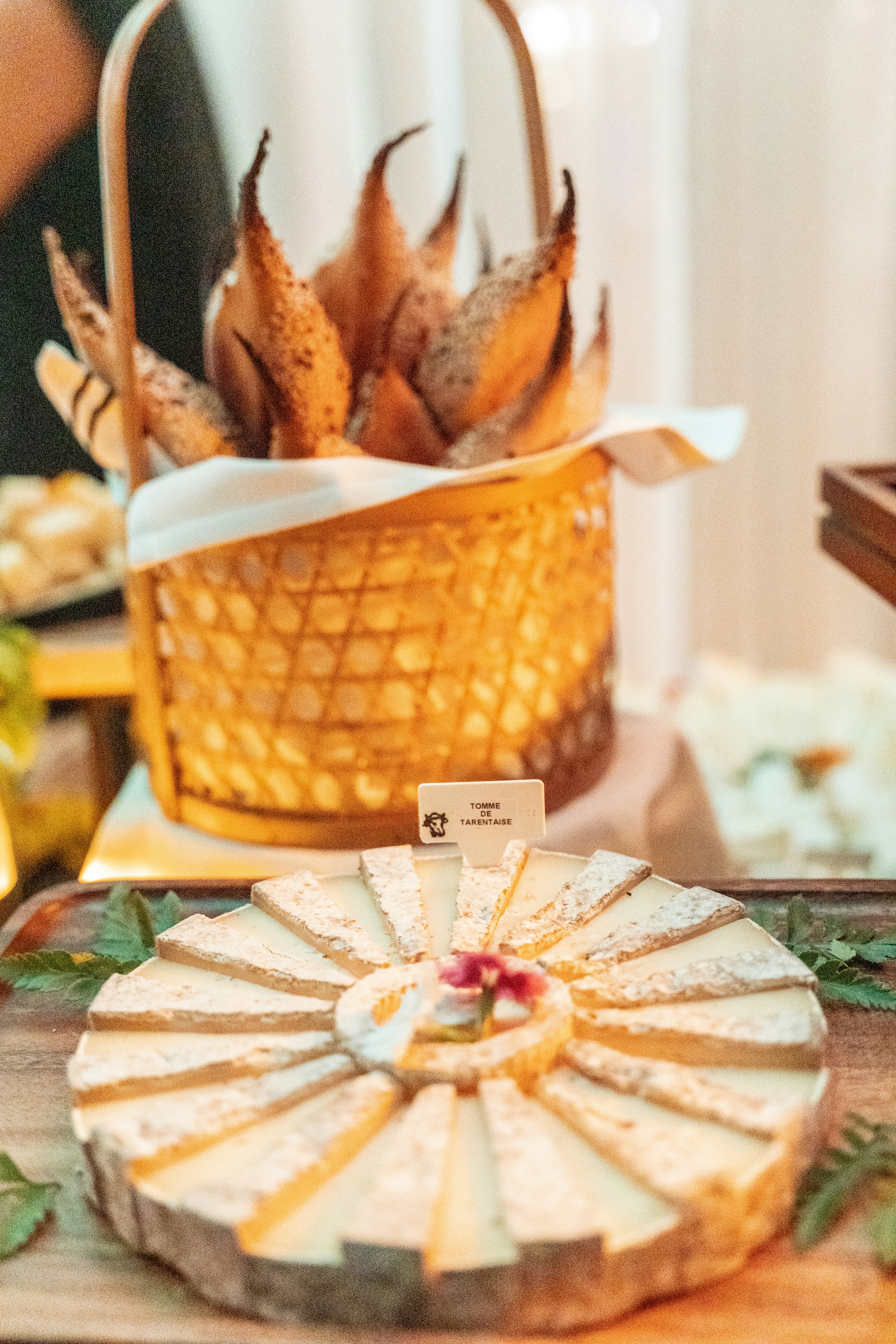Sliced cheese platter with bread basket in background