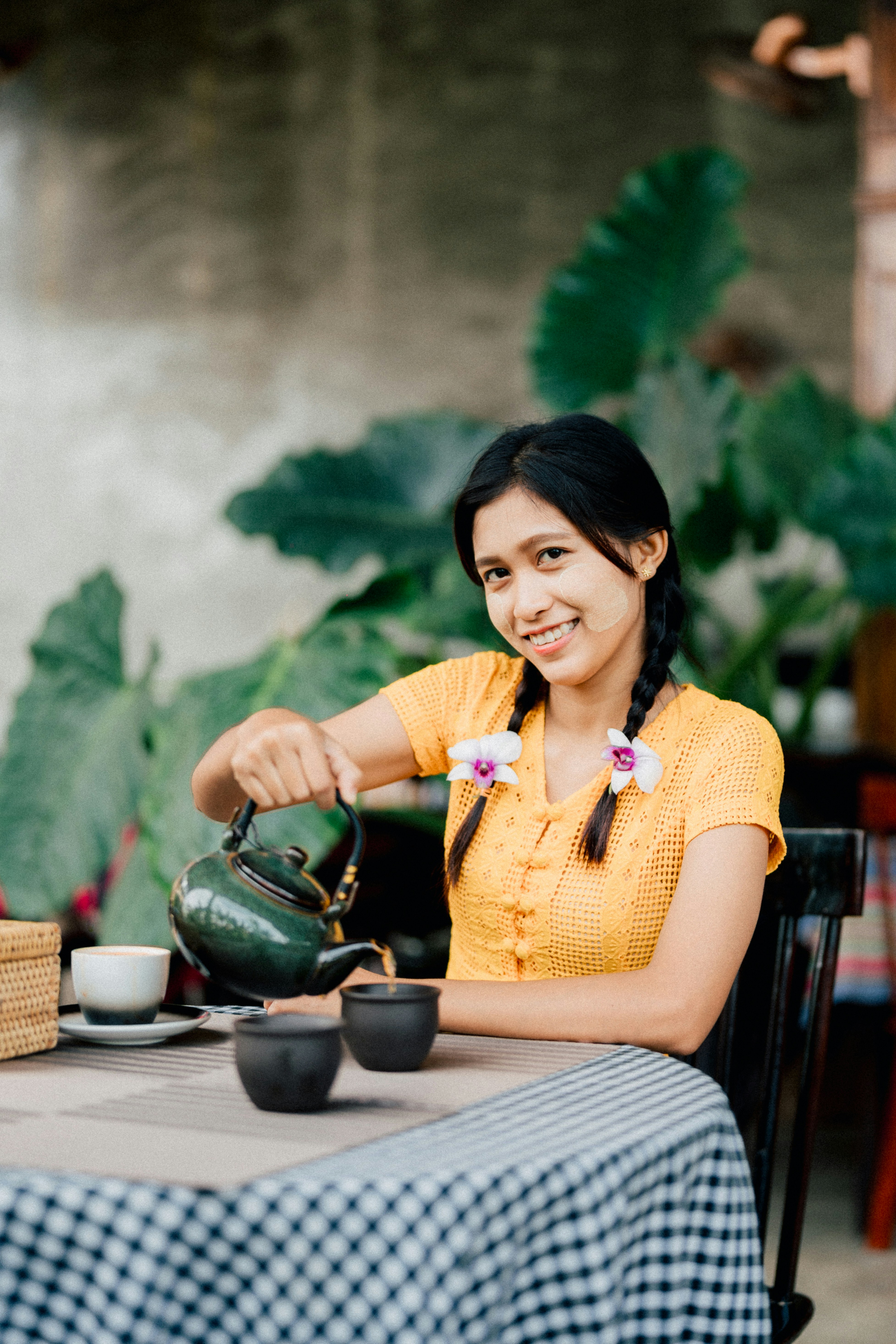 Woman pouring tea at a table with flowers.