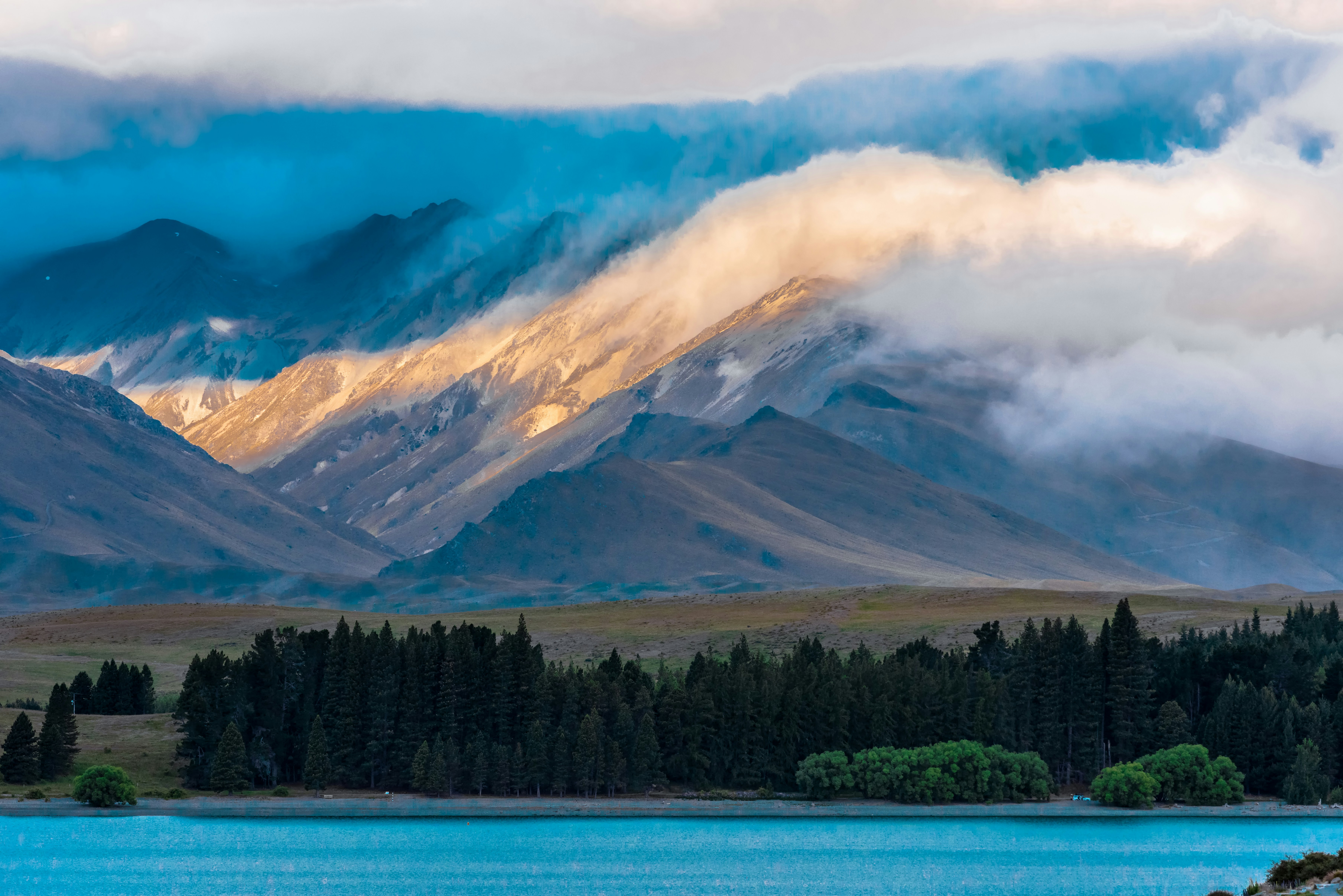 Golden sunlight illuminates misty mountain peaks above a forest.