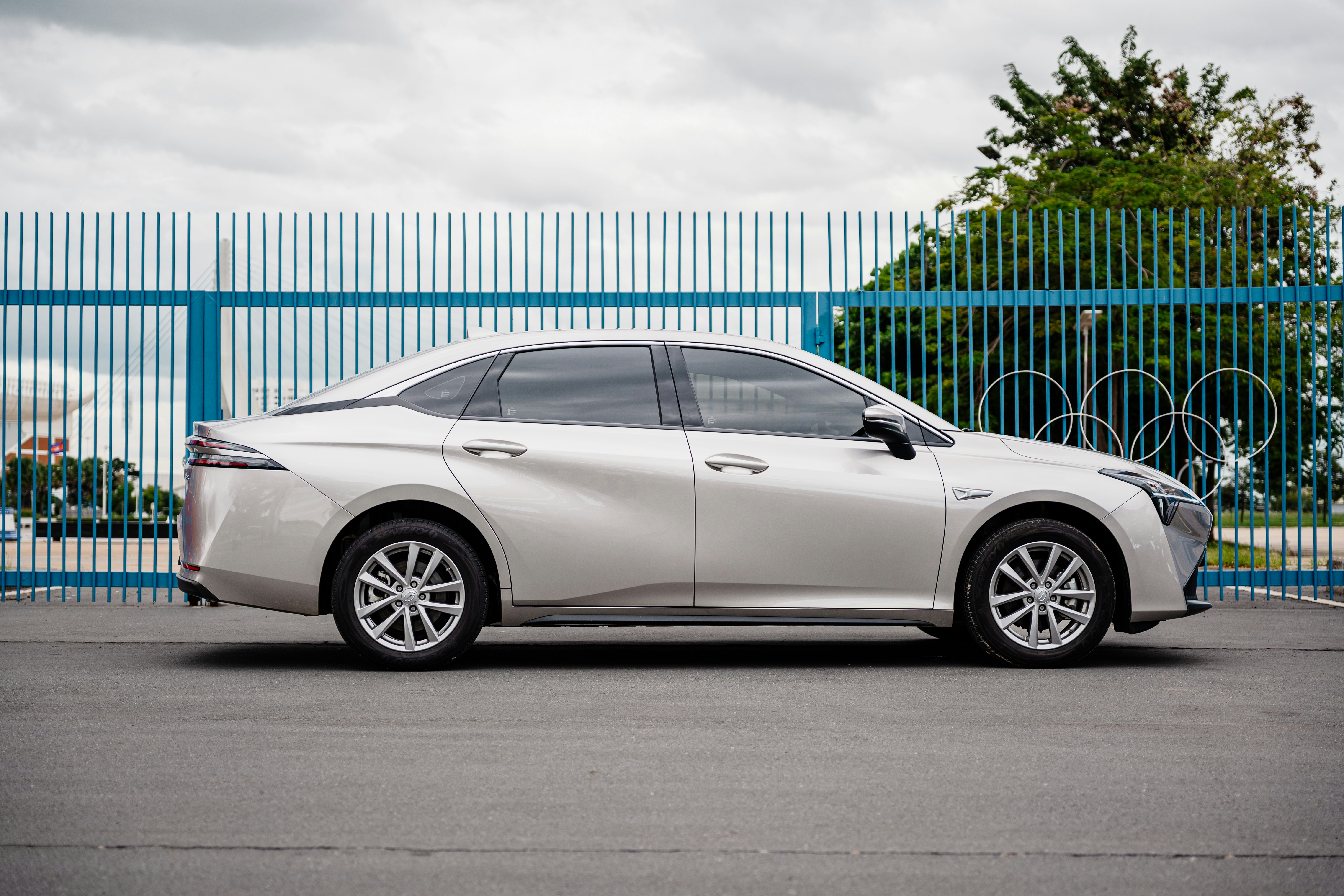 Sedã prateado estacionado perto de uma cerca azul com anéis olímpicos.