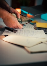 Hands holding cash over desk with papers.