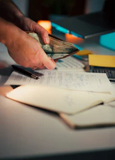 Hands holding cash over desk with papers.