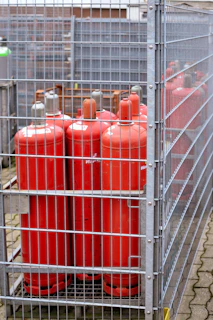 Red propane tanks stored in a metal cage.