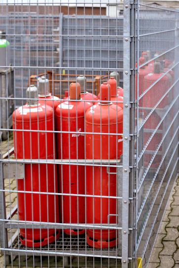 Red propane tanks stored in a metal cage.