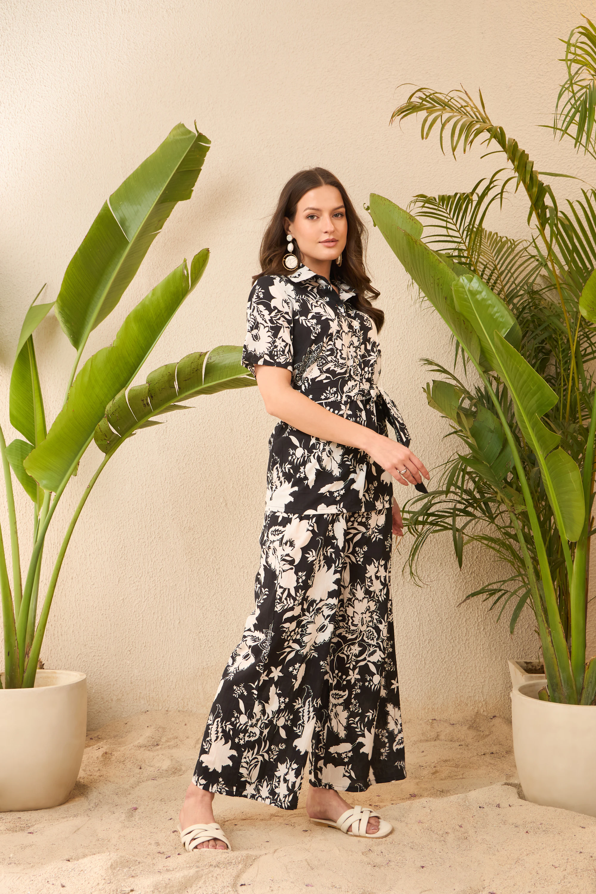 Model in a black and white botanical maxi dress against a cream wall and banana leaves