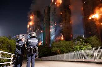 Riot police watch buildings engulfed in flames at night.