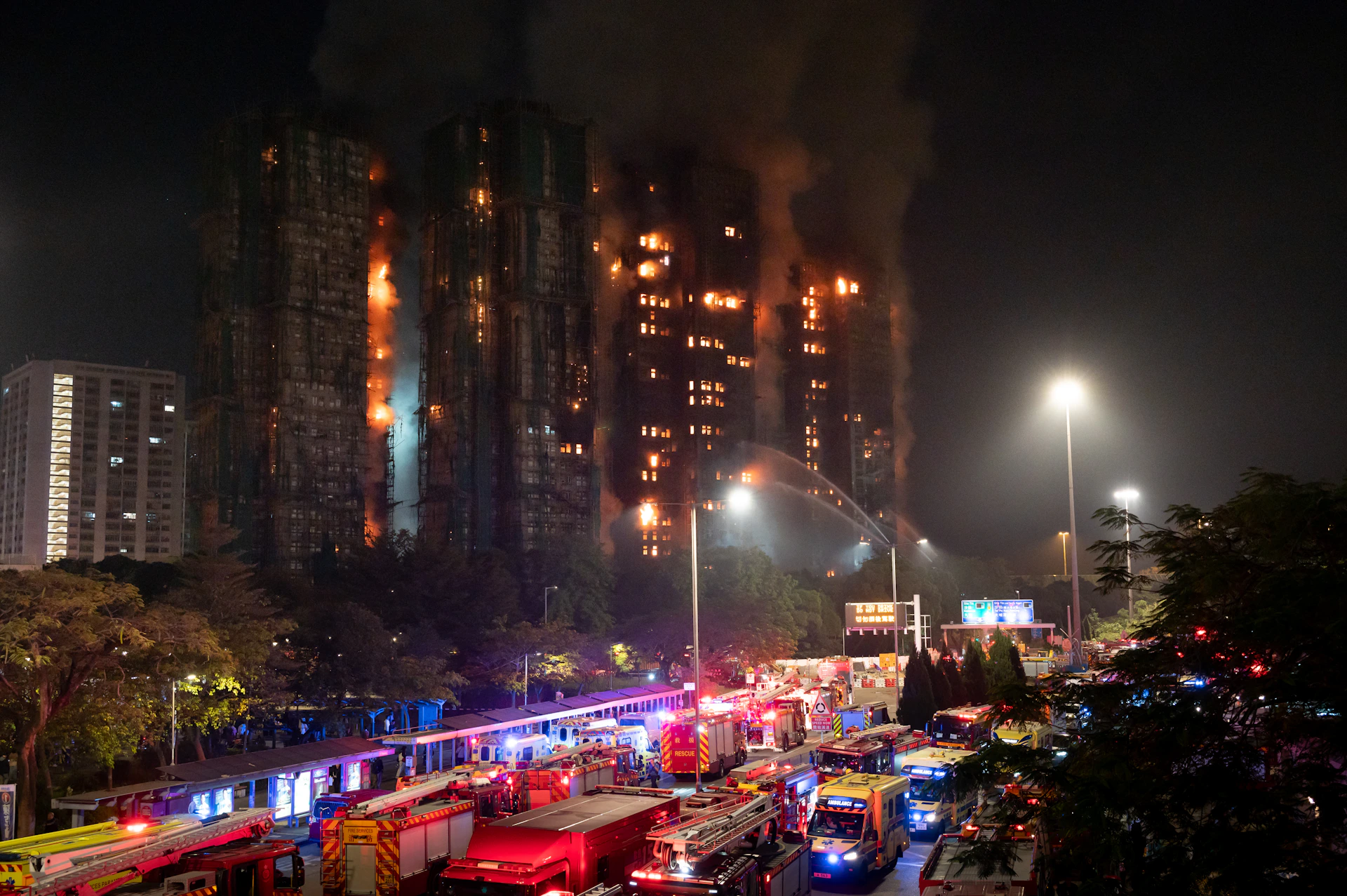 Apartment building engulfed in flames with emergency vehicles below.