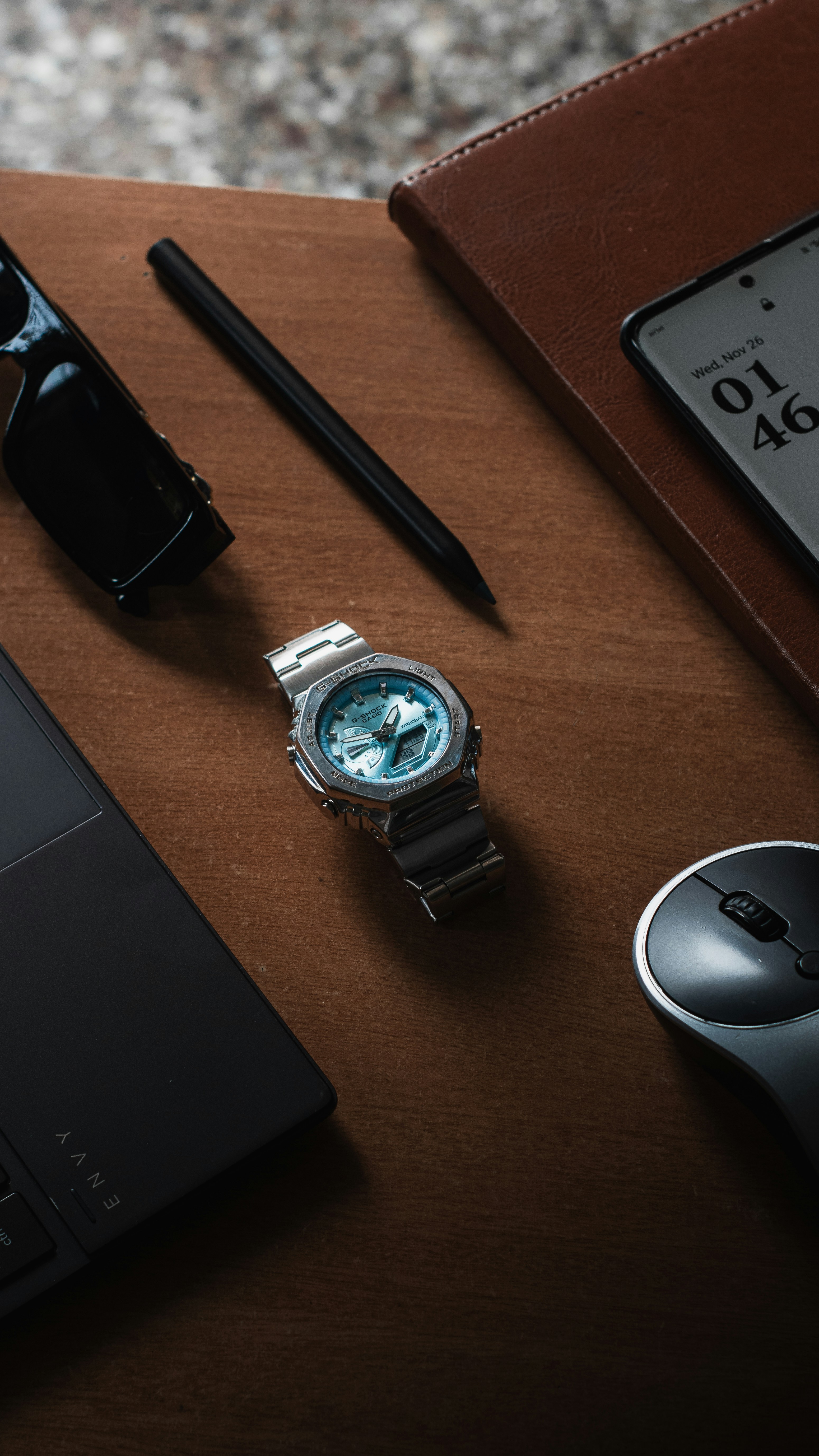 Watch, laptop, sunglasses, pen, mouse, and phone on desk.