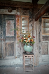 Vase of flowers on a wooden stool near a doorway.
