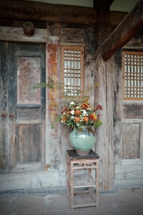 Vase of flowers on a wooden stool near a doorway.