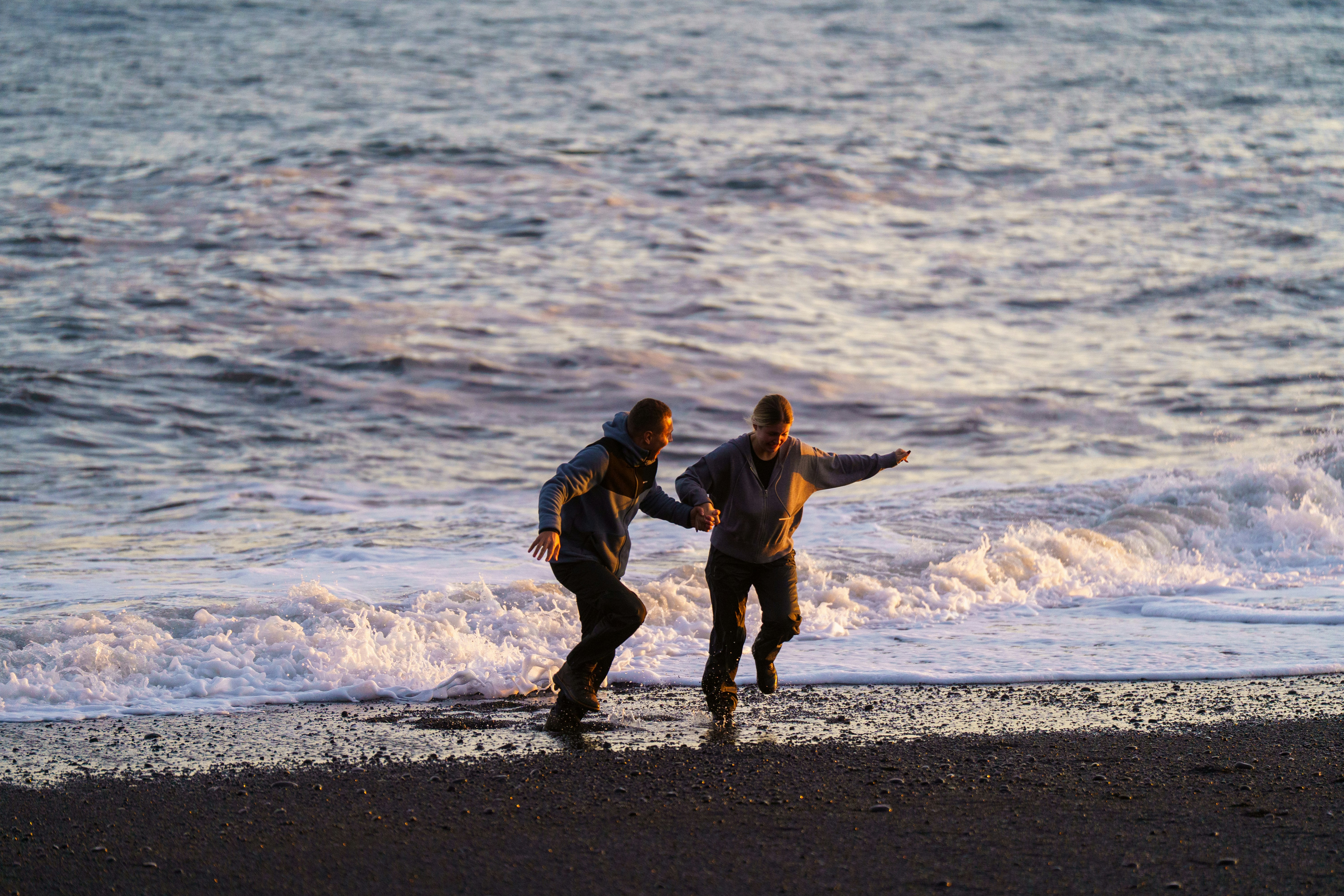 Two people running on a beach at sunset.