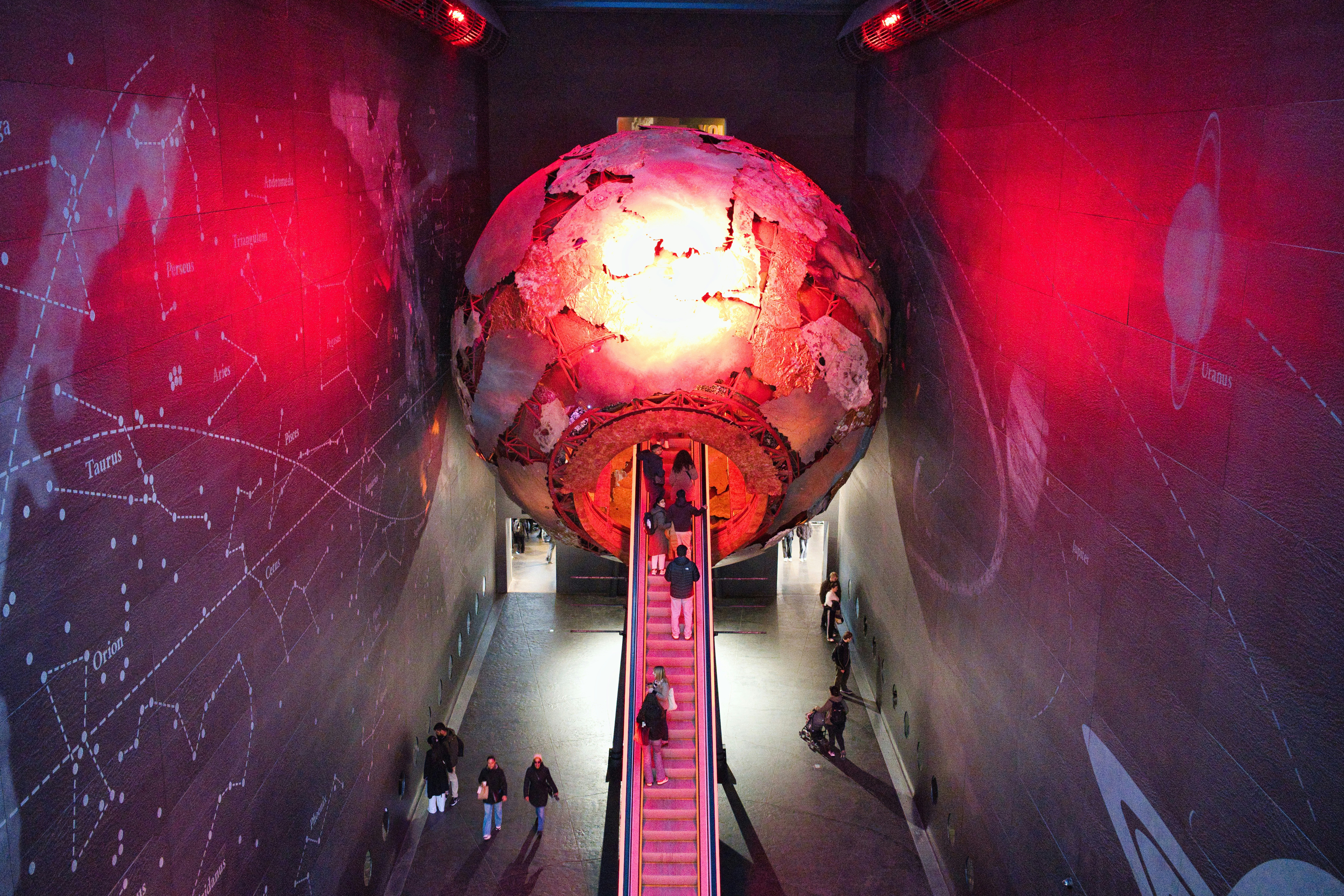 People ascend escalator towards large glowing globe