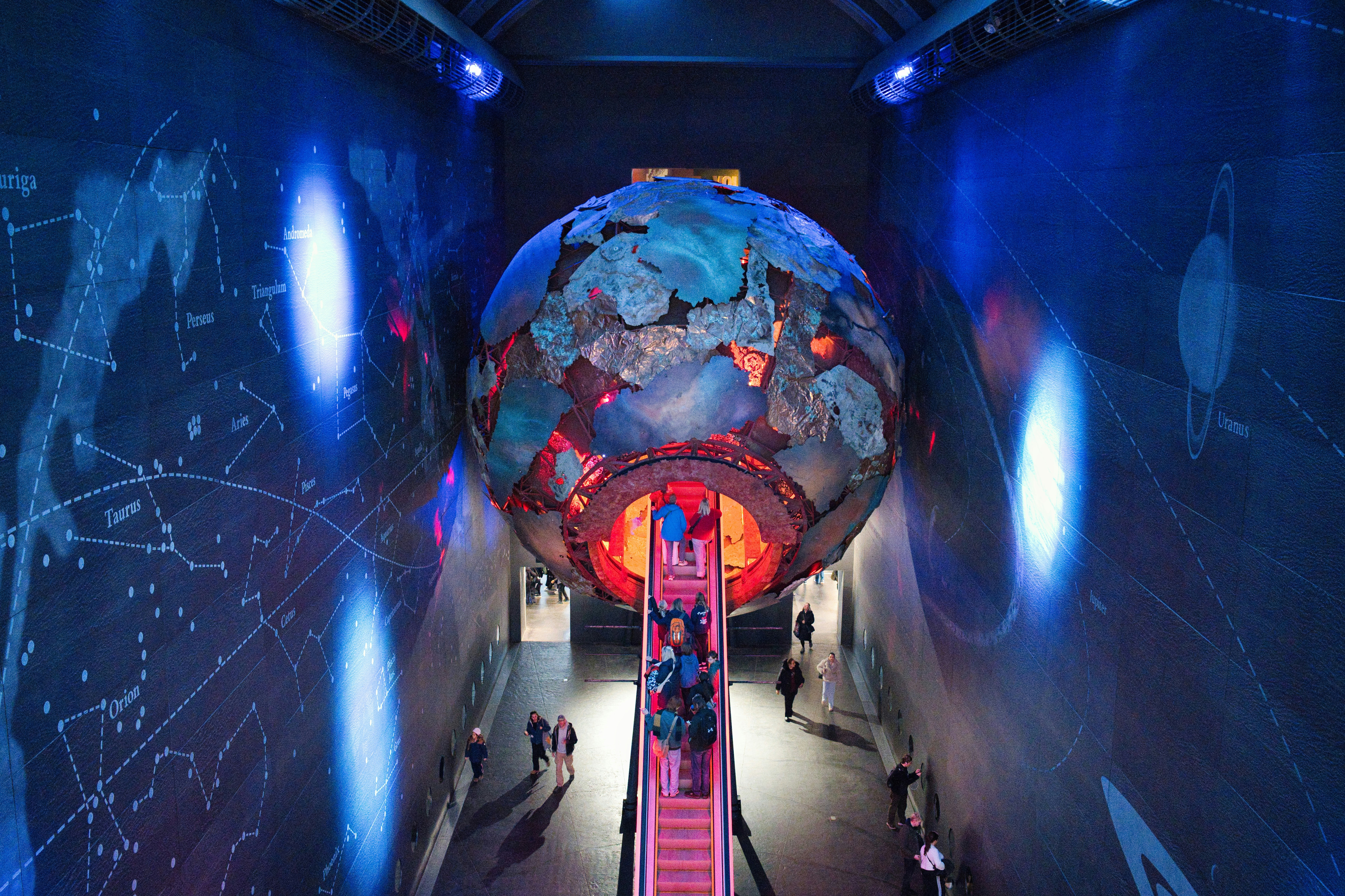 Large glowing globe with people on escalator below.