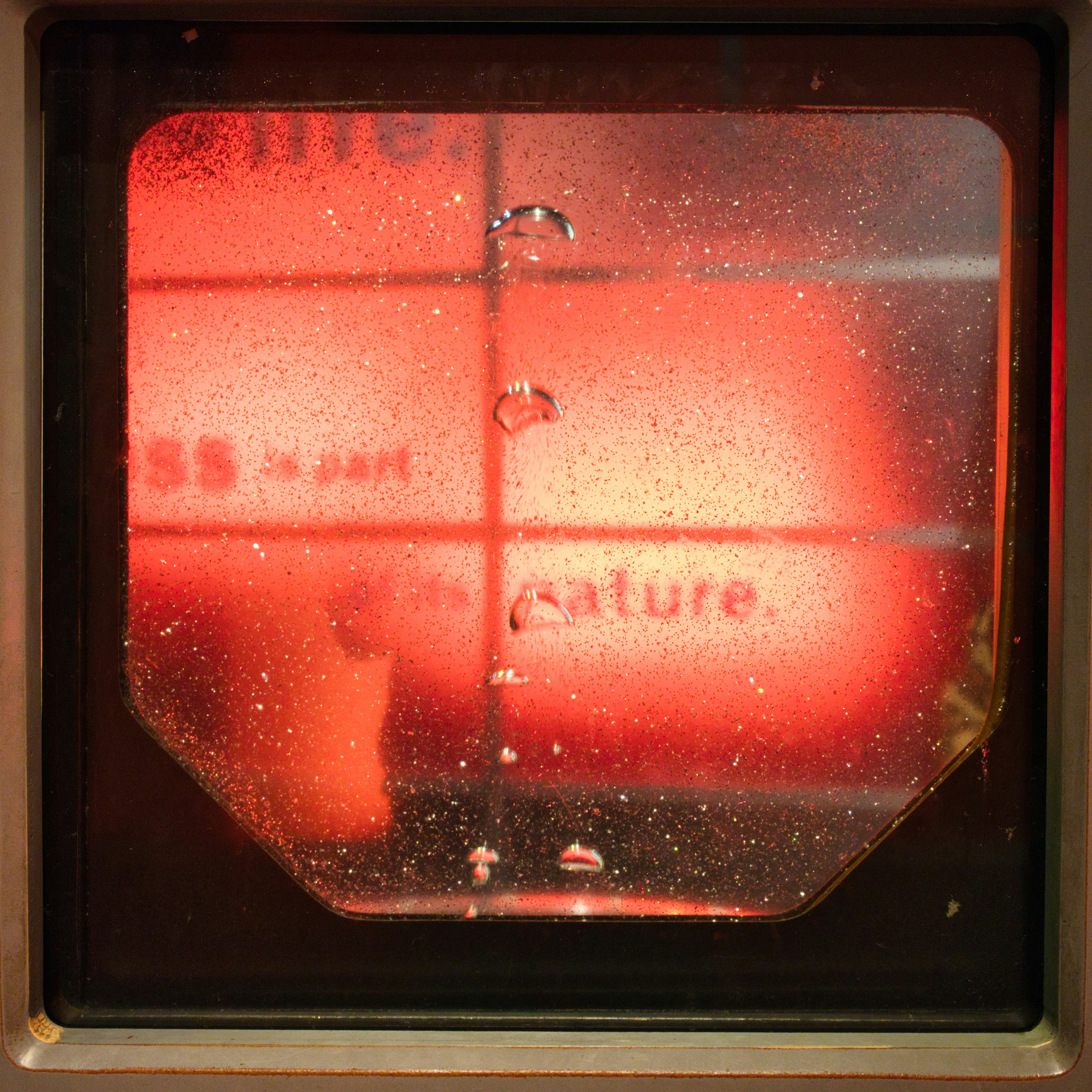 Bubbles rise in red liquid with text behind.