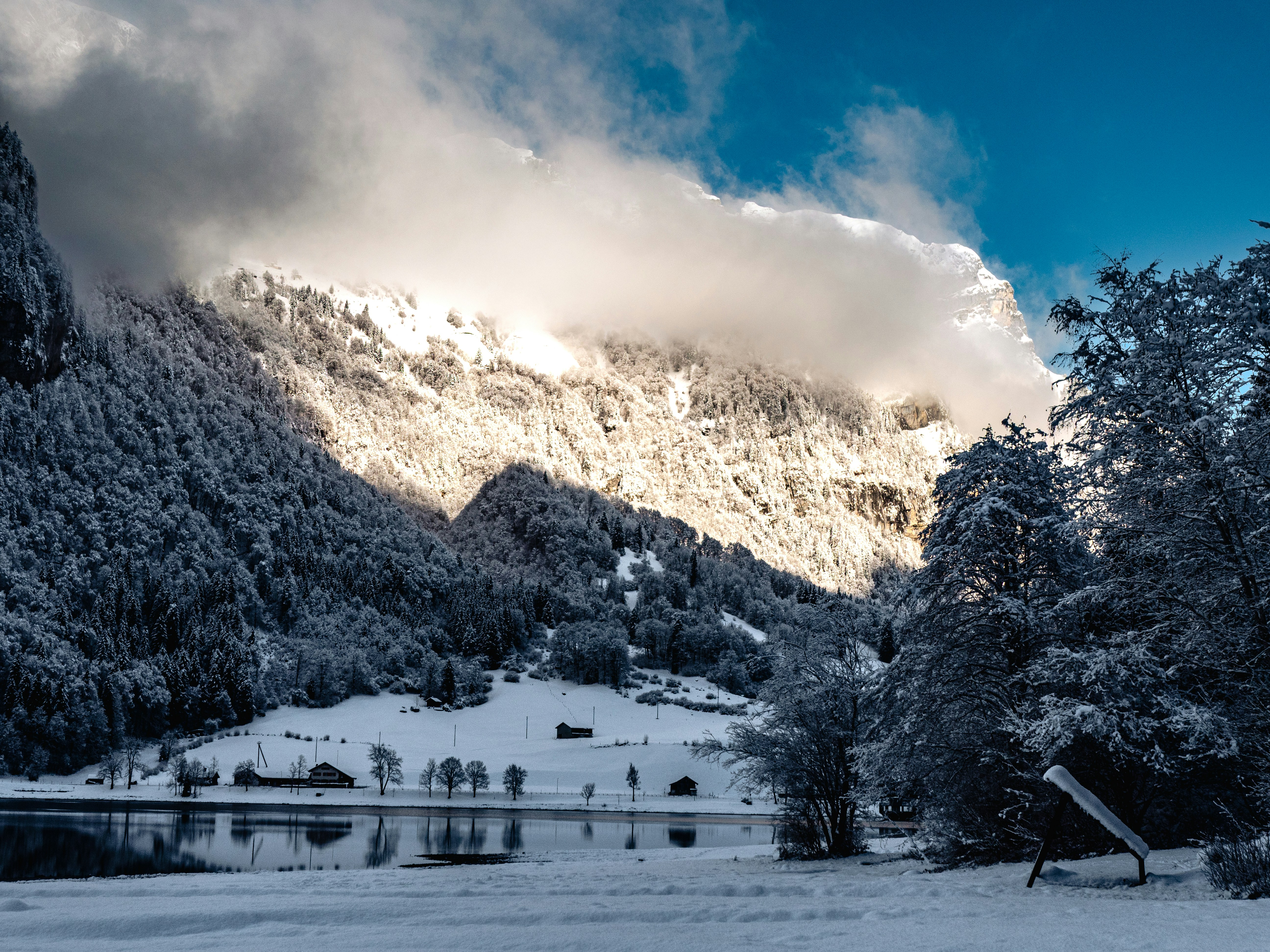 Snowy mountain landscape with sunlit clouds and trees