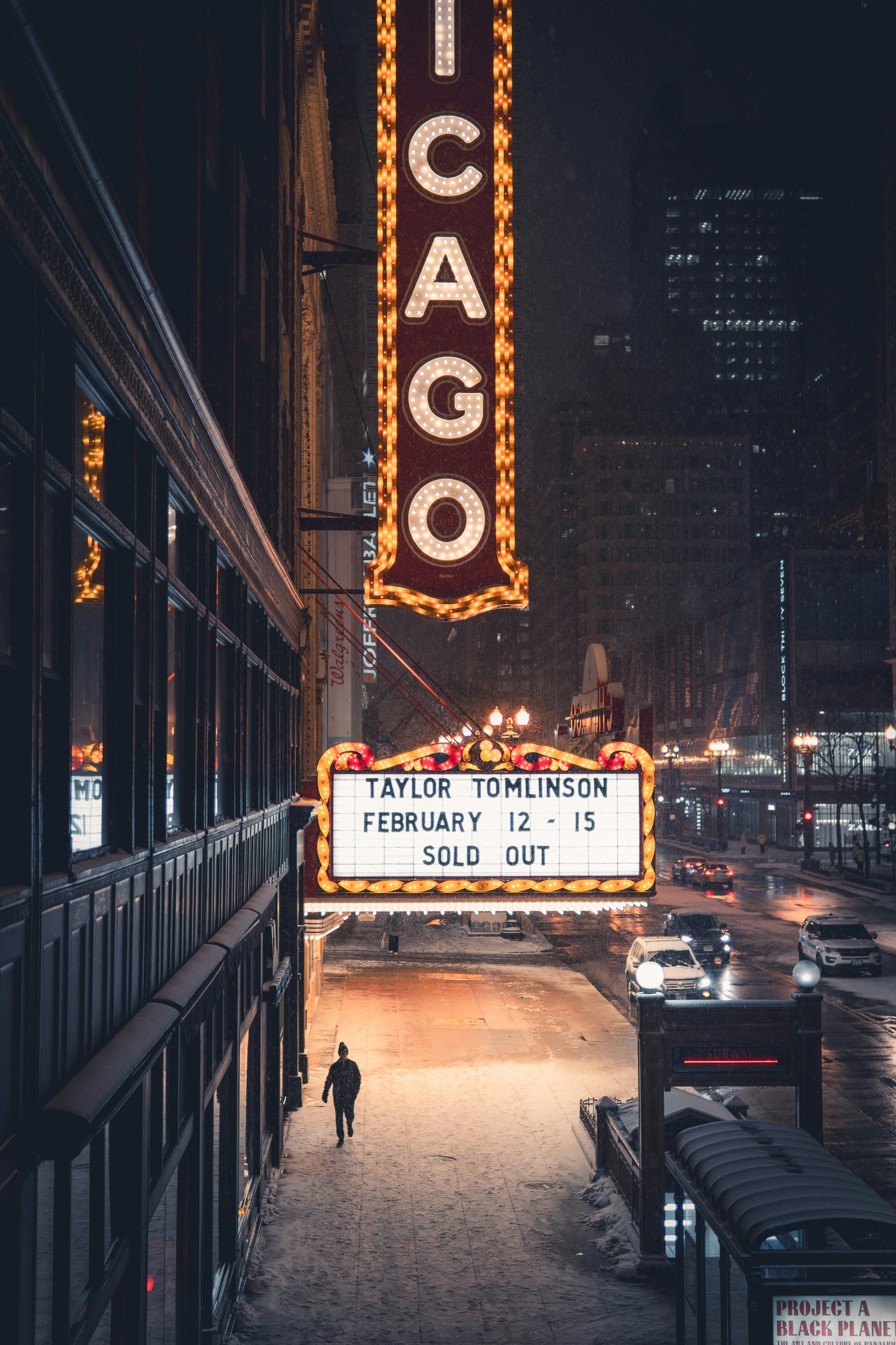 A person walks past a theater marquee at night.