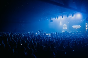 A large crowd watches a concert on a blue-lit stage.