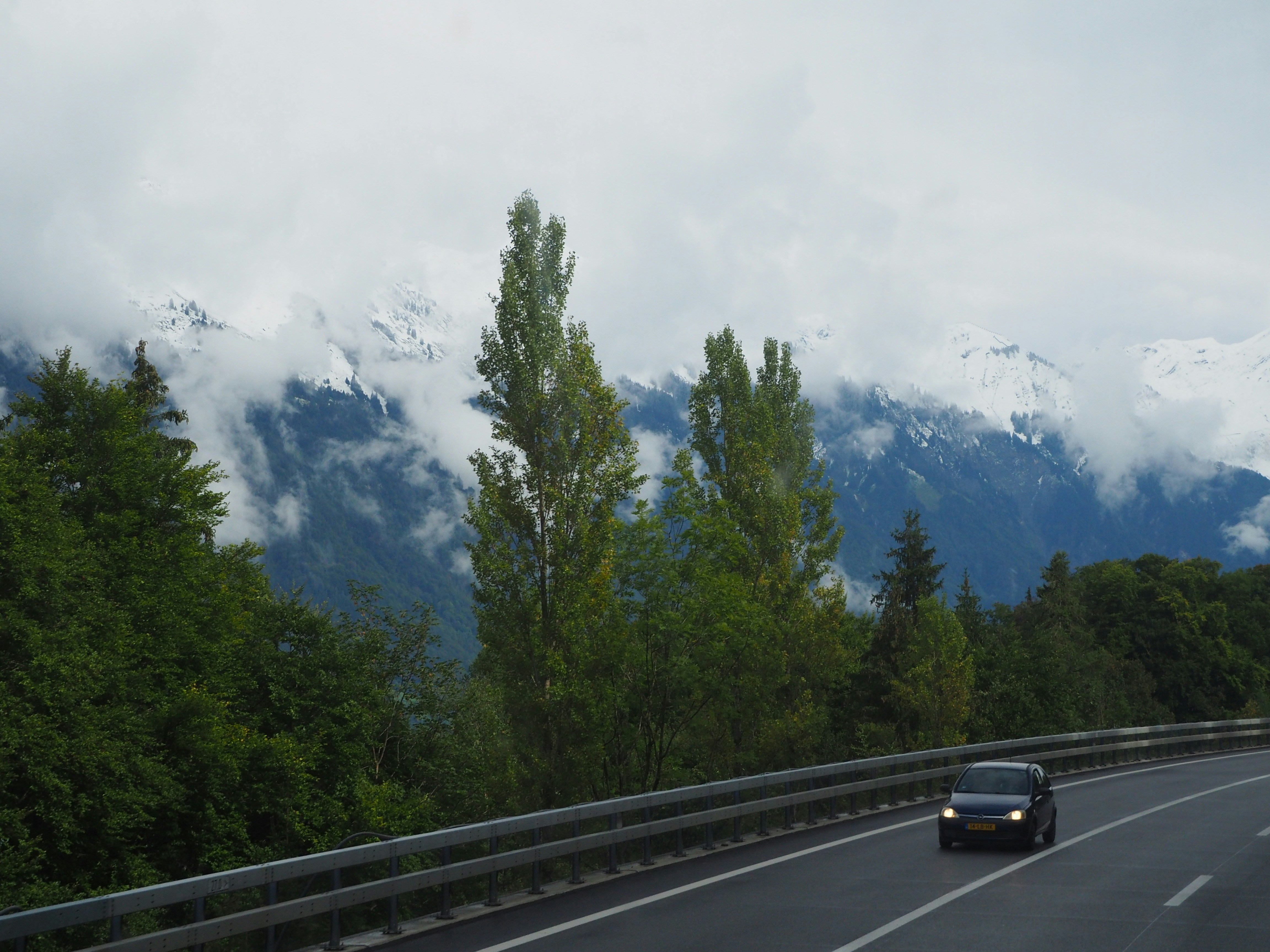 Car driving on highway with snowy mountains behind trees