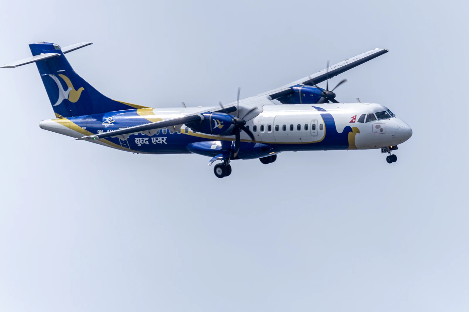 A Buddha Air ATR 72 turboprop in blue and white livery with gold trim, wheels down against a pale sky over Nepal