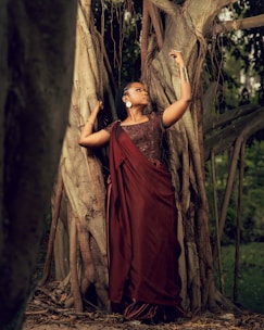 Woman in traditional attire poses by a large tree.