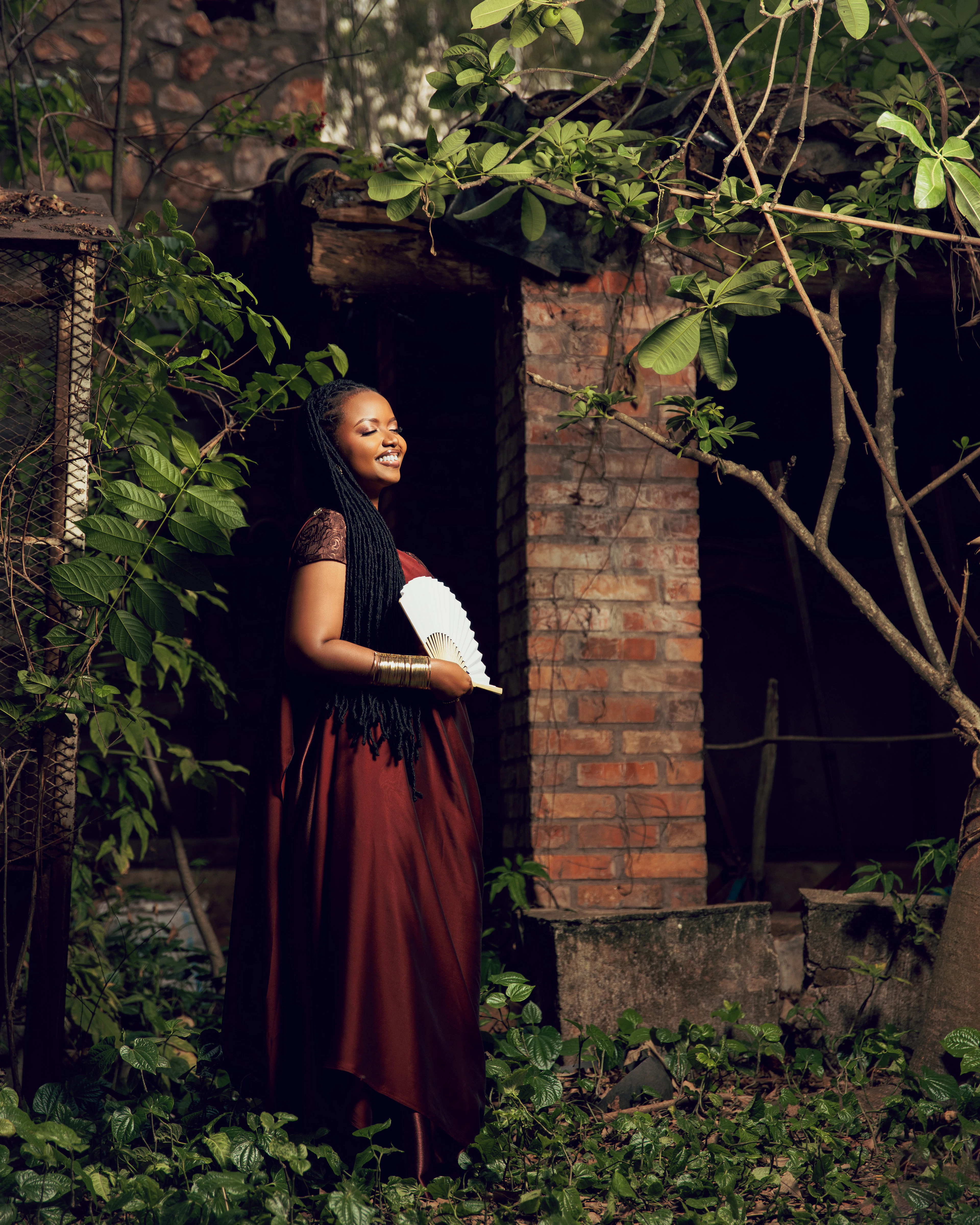 A woman in a long dark red skirt standing in a doorway framed by climbing plants