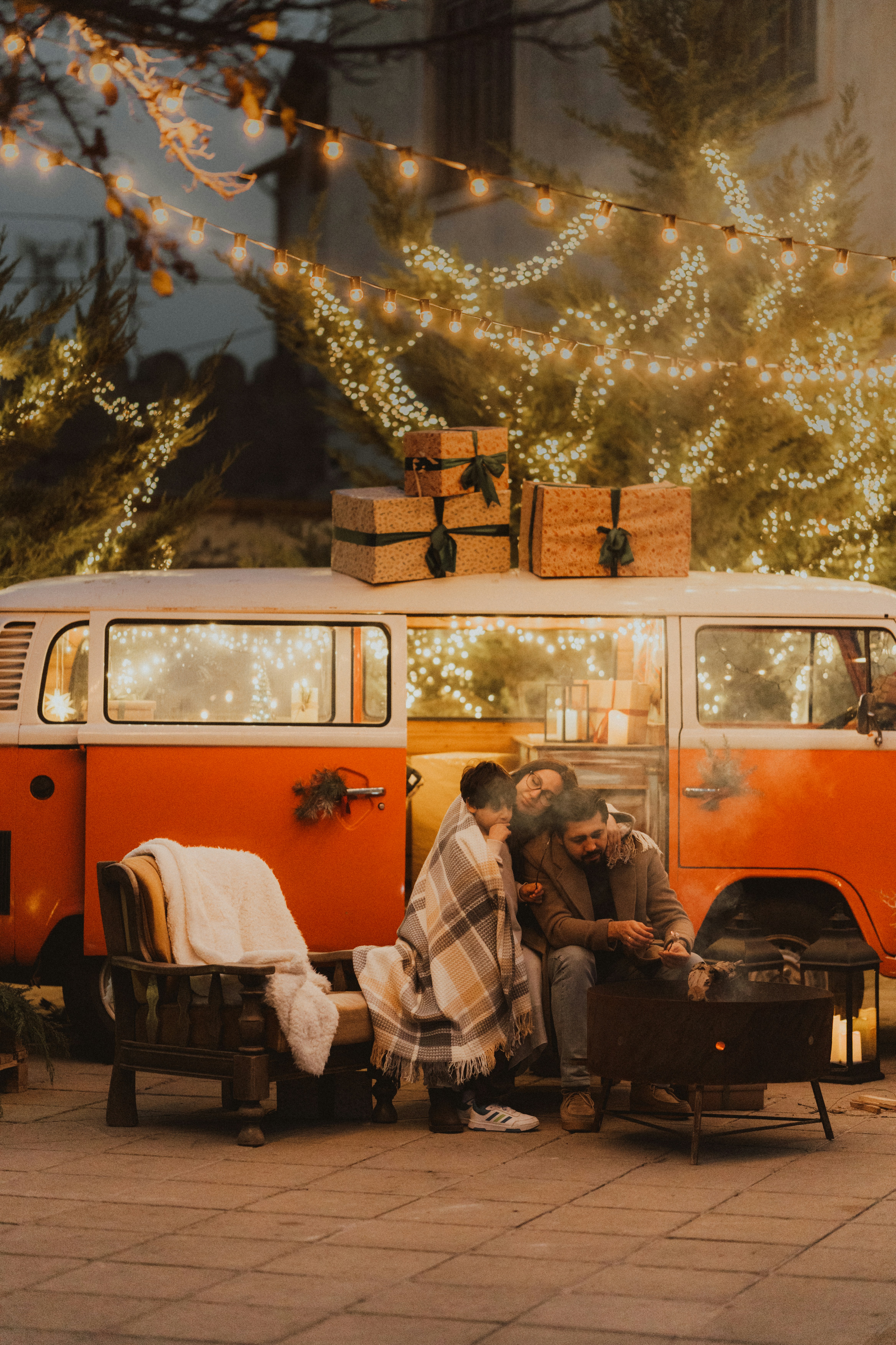 Couple by campfire next to vintage van with christmas lights