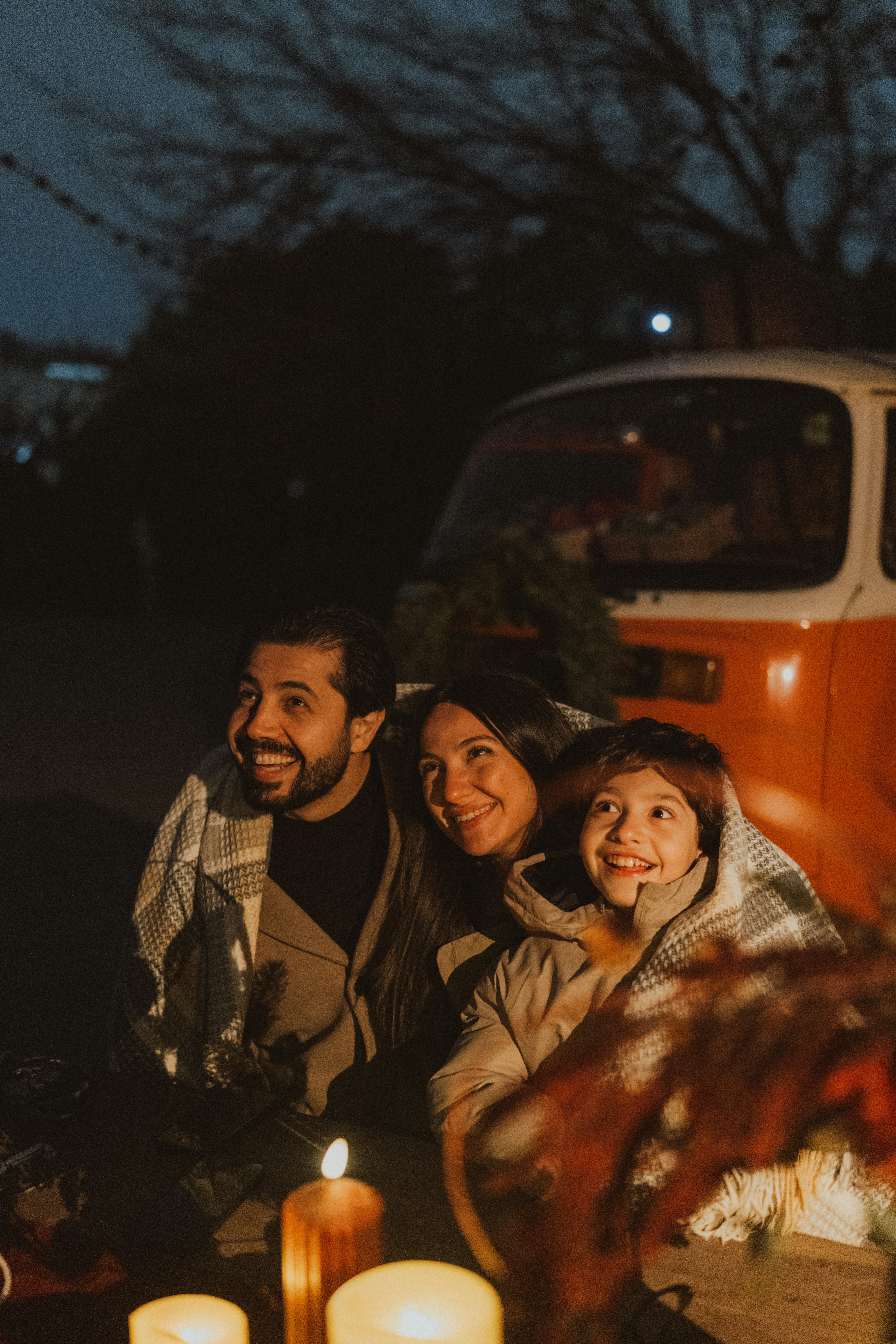 Family wrapped in blanket with camper van at night