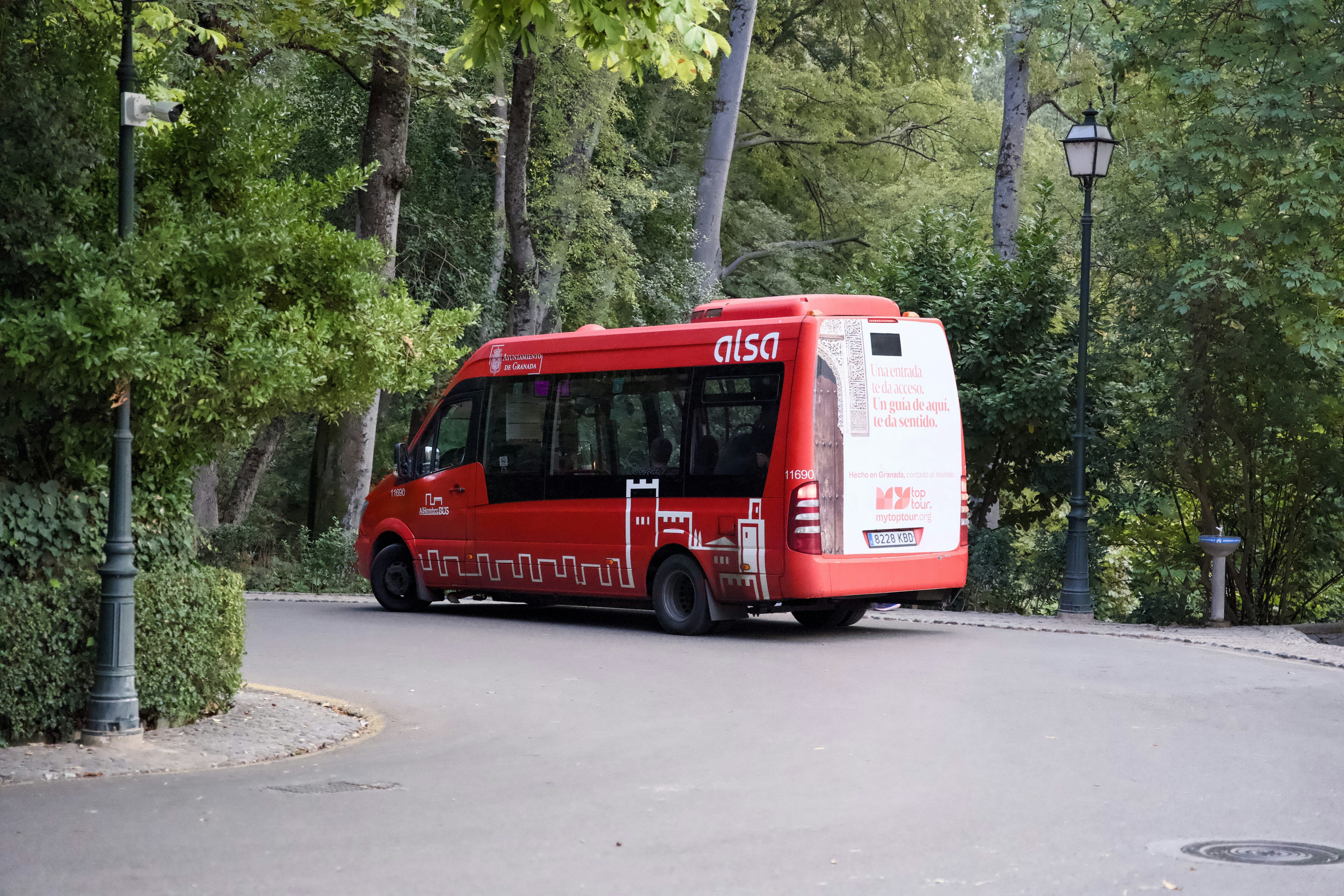 Um ônibus vermelho passa por uma estrada entre árvores.