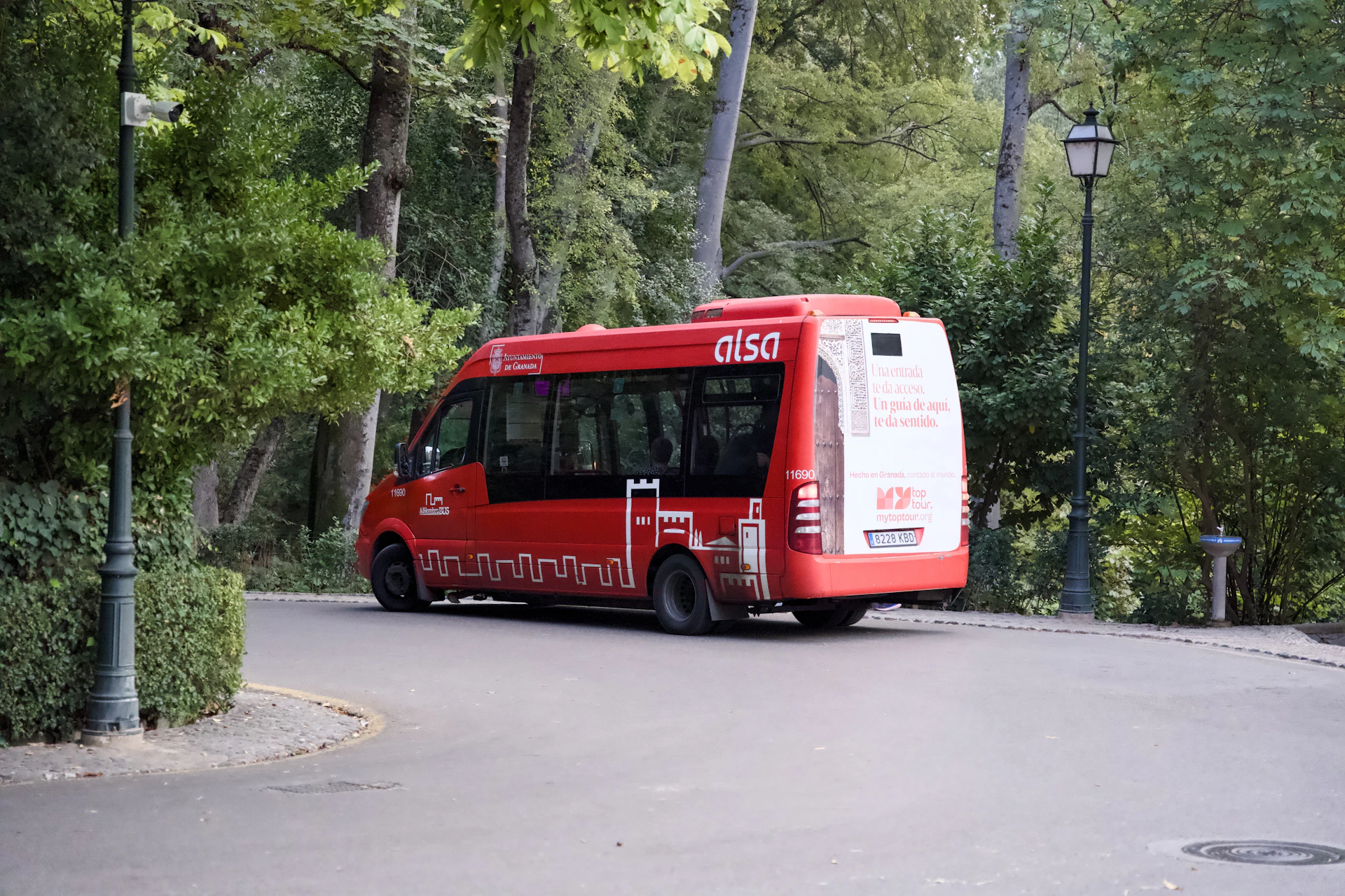 A red bus drives on a road through trees.