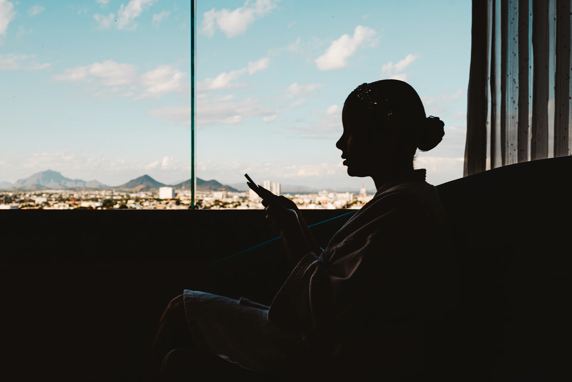 Silhouette of woman using phone with city view.